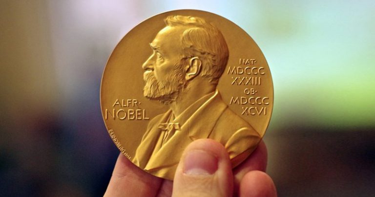 Uma mão segurando a medalha do Prêmio Nobel