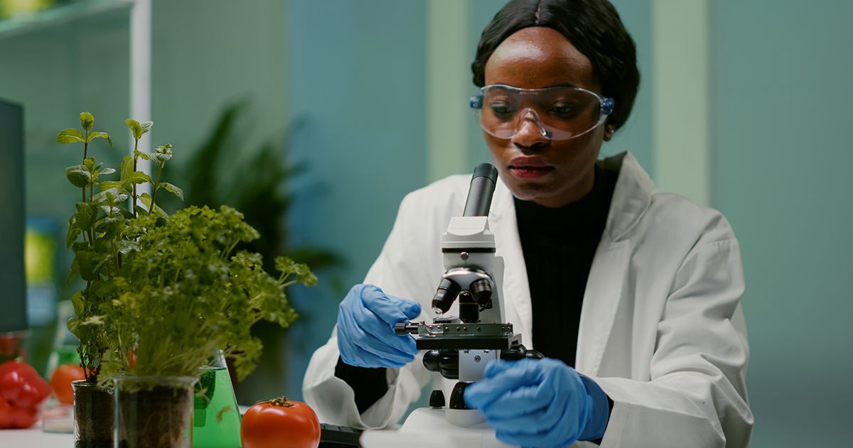 A imagem mostra uma mulher negra manuseando um microscópio