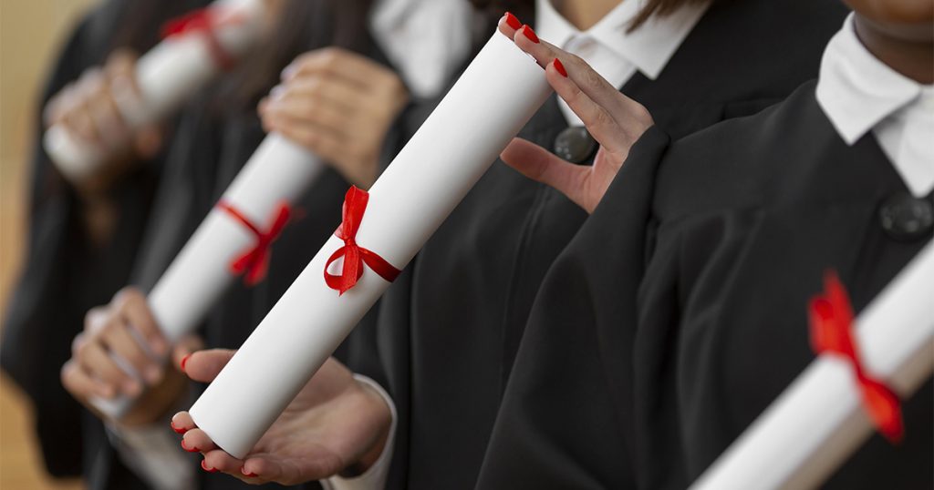 Imagem de estudantes, dos quais só se veem as mãos, que seguram diplomas