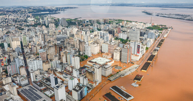 Vista aérea das enchentes no Rio grande do Sul, com prédios e rua alagadas com água na cor de barro