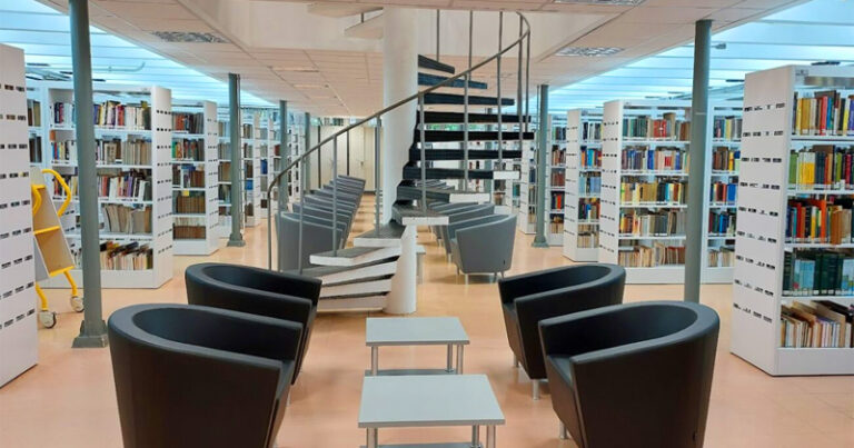 Biblioteca da USP, com prateleiras modernas de livros, poltronas e mesas, e uma escada espiral ao meio que leva ao andar superior