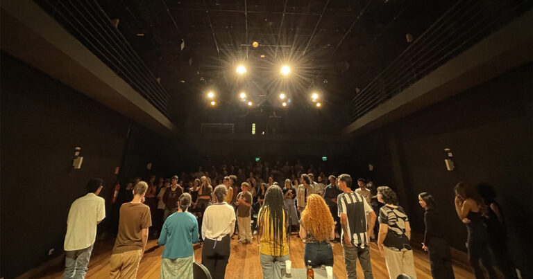 Alunos da USP reunidos em círculo num palco, olhando uns para os outros