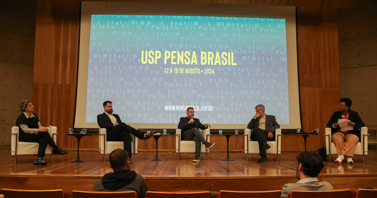 Duas mulheres e três homens, sentados em um semicírculo, em um palco. Atrás um telão com os dizeres "USP Pensa Brasil" - 12 a 16 de agosto, 2024