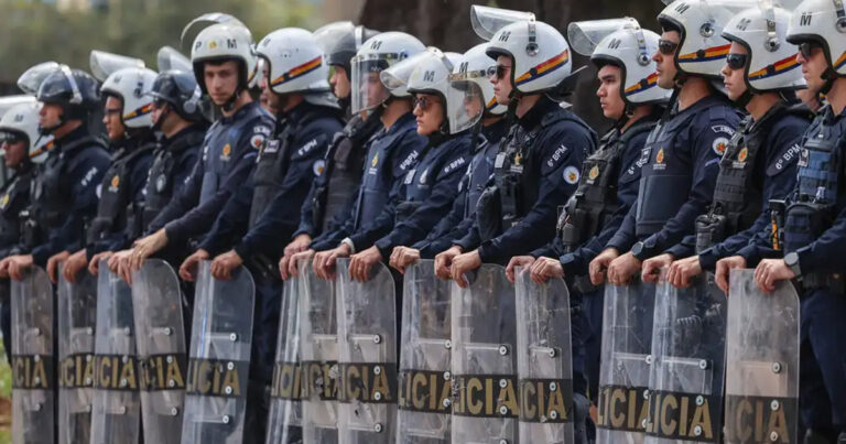 Imagem mostra policiais em fila, um ao lado do outro, com escudo a frente do corpo