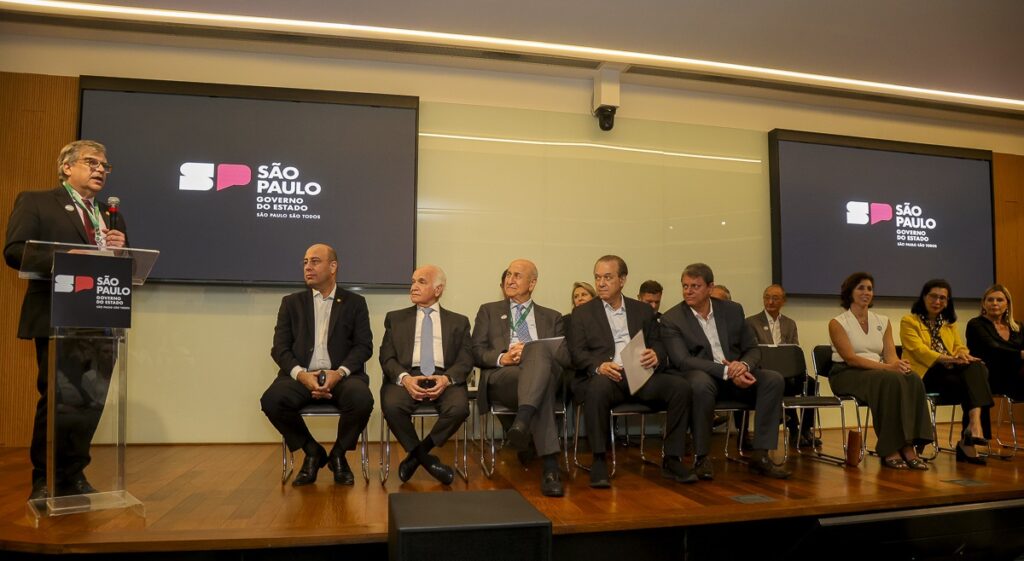 No palco do auditório, o reitor Carlos Gilberto Carlotti Junior discursa, em pé, enquanto as demais autoridades permanecem sentadas.