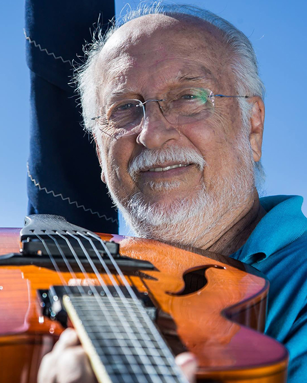 Homem de barba e de óculos segurando um violão.