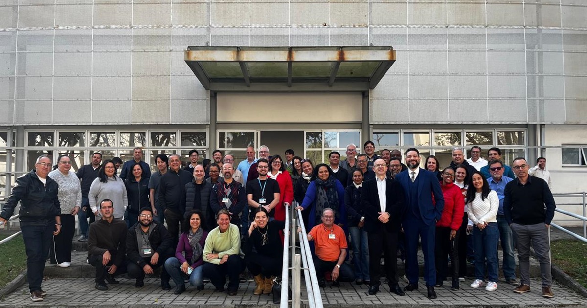 Grupo de homens e mulheres sorriem diante da fachada de um prédio