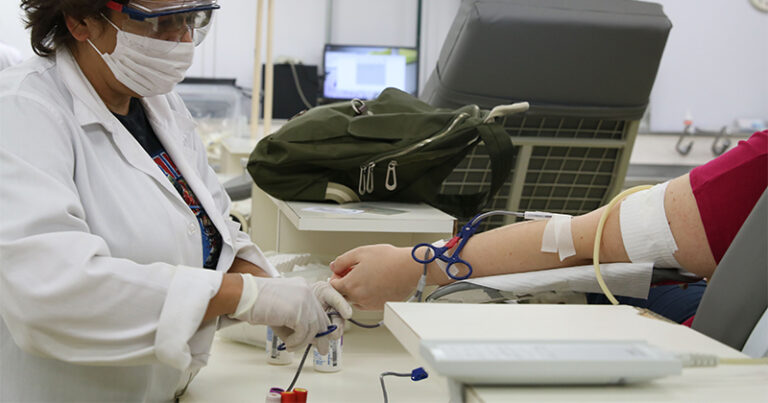 Enfermeira sentada ao lado de paciente controlando a doação de sangue