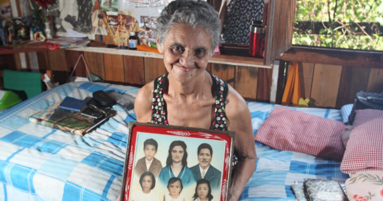 Mulher idosa, de cabelos brancos, segurando quadro com retratos de familiares