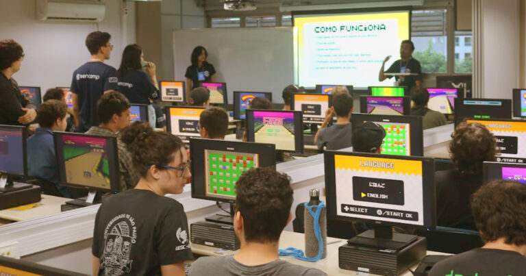 Várias pessoas numa sala de aula, sentadas em frente a computadores acessando viodeogames