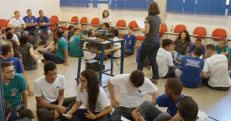 Sala de aula com estudantes sentados no chão em grupo para fazer uma atividade educativa