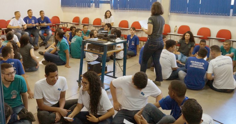 Sala de aula com estudantes sentados no chão em grupo para fazer uma atividade educativa