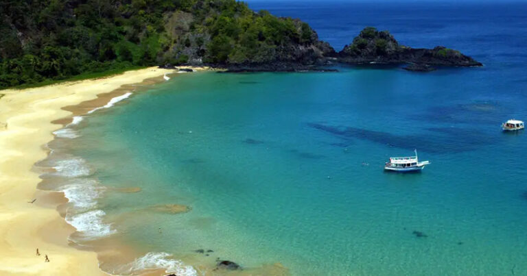 Foto aérea de uma praia e do aceano com uma parte de terra com vegetação