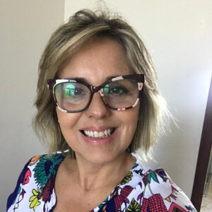 Mulher branca de óculos, cabelos claros e curtos, sorrindo e com roupa estampada 