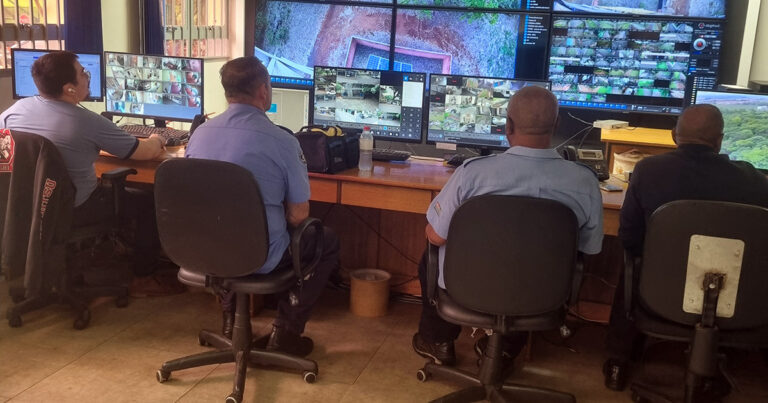 Na imagem sala de monitoramento com várias pessoas sentadas de costas e todas de camisa azul, na frente delas, várias telas com imagens do campus da USP em Ribeirão Preto