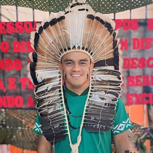 Imagem: Homem branco usando um grande cocar indígena e trajando camisa verde