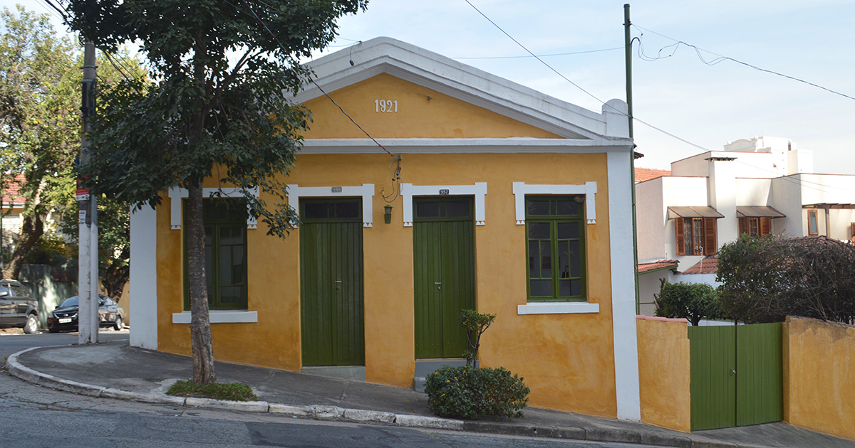 Uma casa amarela com portão, portas e janelas verdes.