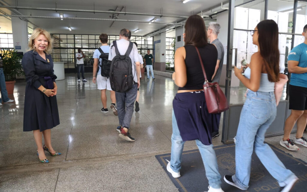 Mulher com vestido azul observa a entrada de estudantes em um prédio