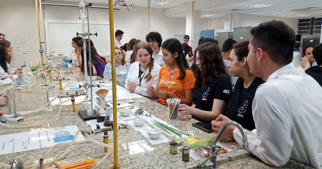 Imagem traz vários alunos em volta de uma mesa em laboratório de pesquisa, mexendo em vários equipamentos 