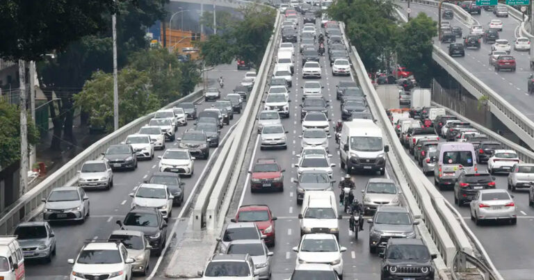 Imagem de vias congestionadas por centenas de veículos, que se espalham, ocupando todos os espaços, por um complexo viário típico de uma cidade grande como São Paulo