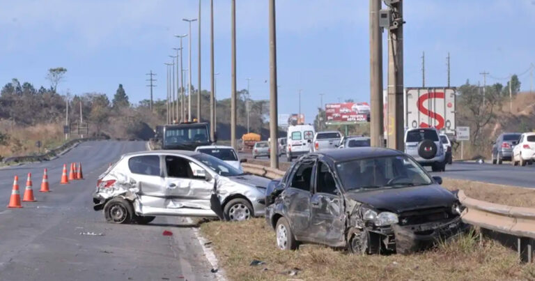 Imagem de um acidente automobilístico envolvendo dois veículos, um de cor prata e outro azul, que estão no canteiro central de uma via urbana