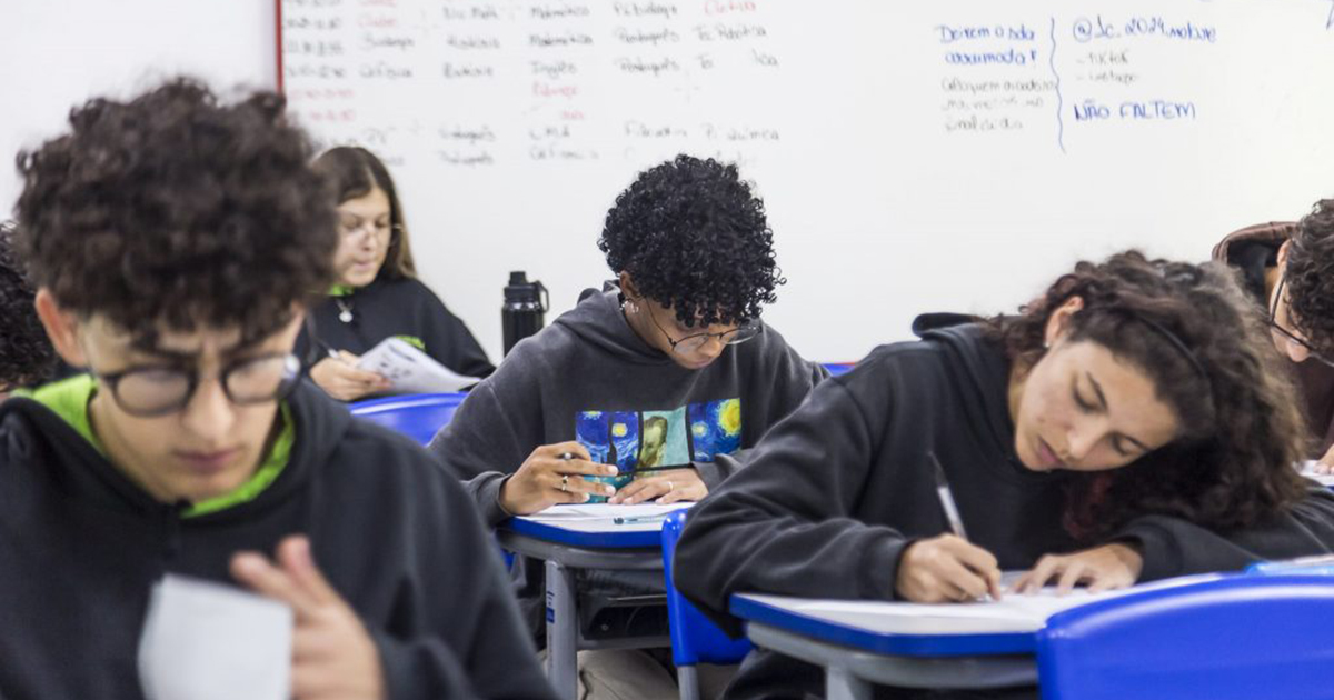 Sala de aula em que aparecem vários estudantes fazendo suas tarefas