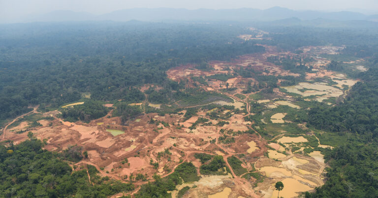 Foto feita de avião sobrevoando uma área completamente devastada pelo garimpo com a região desmatada sendo visível o barro e o rio destruído