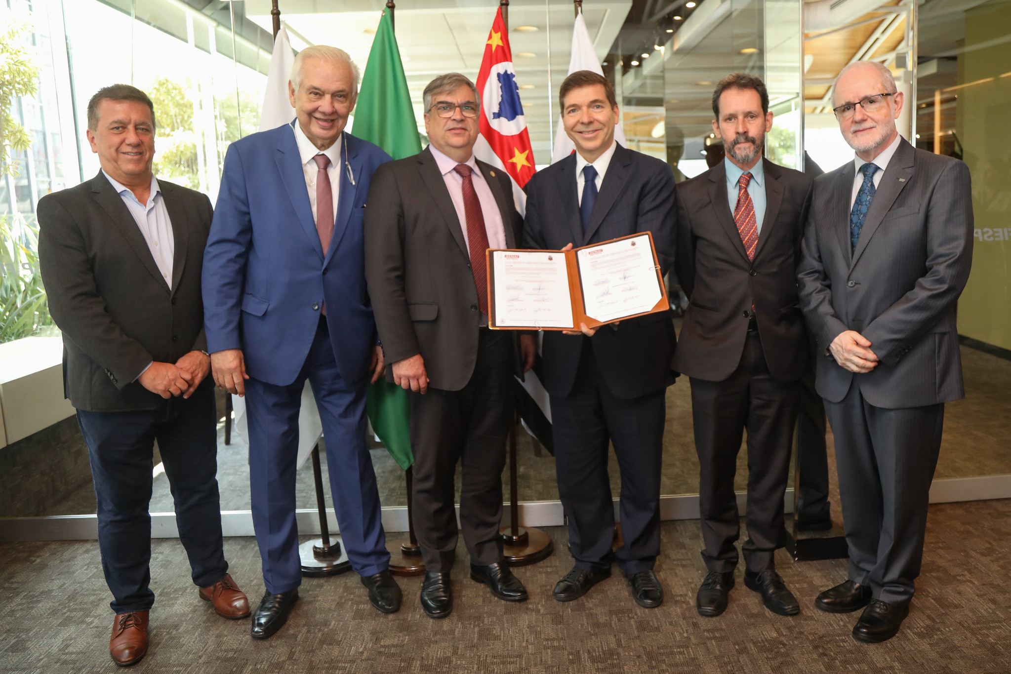 Grupo de homens de terno posam mostrando uma pasta com documento