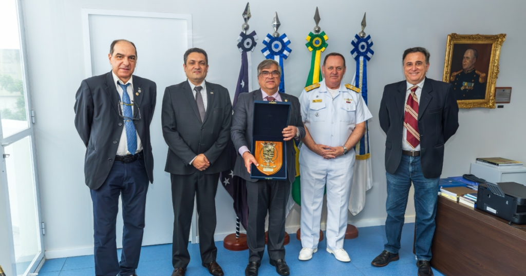 Grupo de homens posa para a foto de pé na frente de uma série de bandeiras