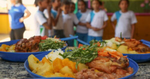 três pratos com merenda escolar e crianças ao fundo