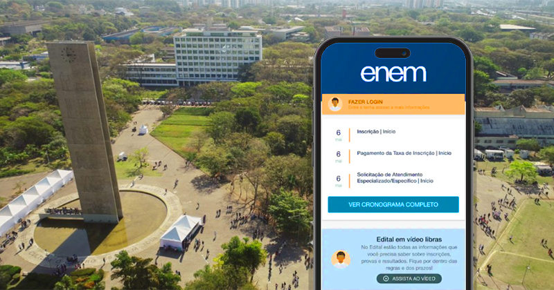 Foto aérea do campus da USP com uma torre com um relógio no topo, uma praça e ao fundo um prédio com oito andares