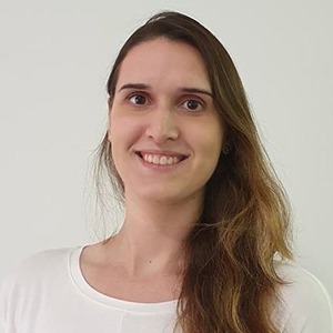 Mulher branca, cabelos escuros, sorrindo para a câmera e vestindo camiseta na cor branca