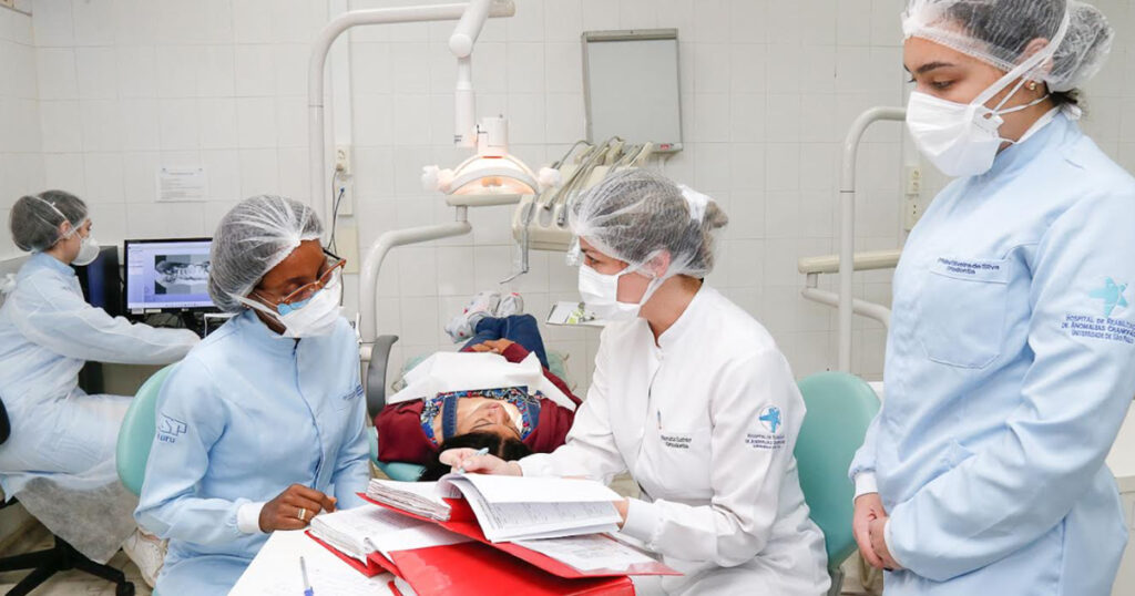 Quatro pessoas atendendo em um hospital, duas delas examinando um paciente deitado