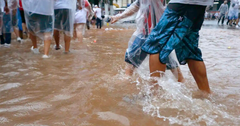 Imagem com foco na perna de pessoas caminhando em águas com barro de enchentes