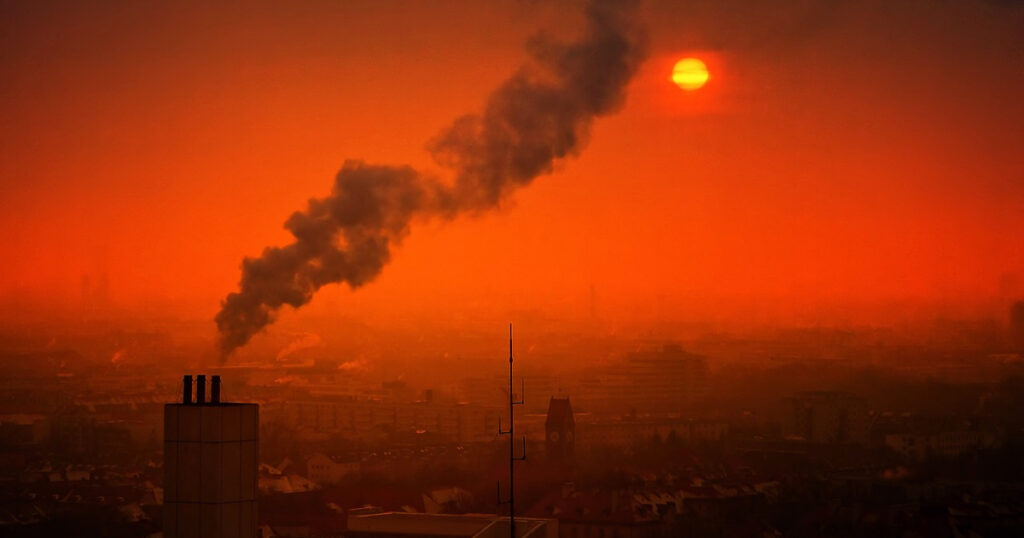 Imagem aérea de cidade ofuscada pela fumaça de poluição e um pôr do sol avermelhado