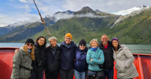 Equipe de oito cientistas num barco e ao fundo montanhas com neve