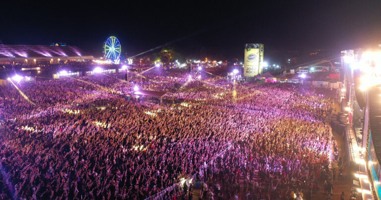 Imagem aérea noturna do Festival João Rock, mostrando milhares de pessoas que acompanham os shows nos palcos do evento