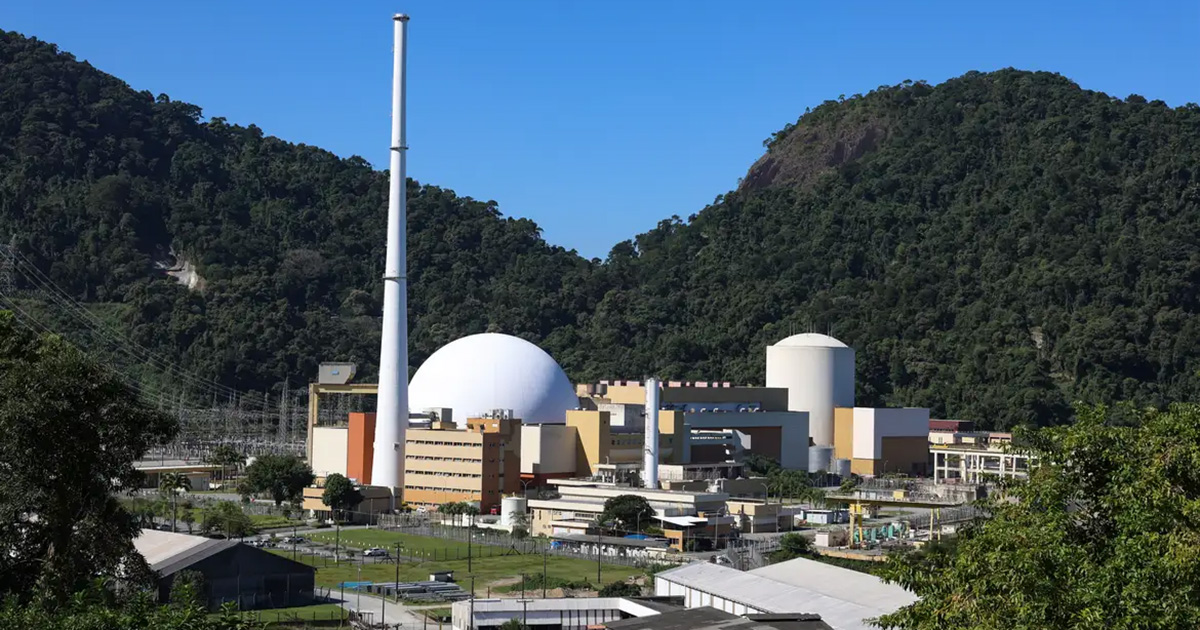 Imagem é uma fotografia colorida que mostra a usina nuclear Angra 1, ao fundo, grande área verde