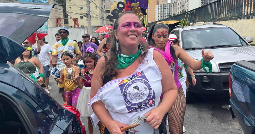 Mulher sorrindo brincando o carnaval numa rua.