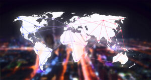 Silhueta do mapa-múndi contornado por imagens gráficas de pontos e linhas interconectados, formando uma rede de conexões. Ao fundo, a visão borrada de luzes de uma cidade à noite