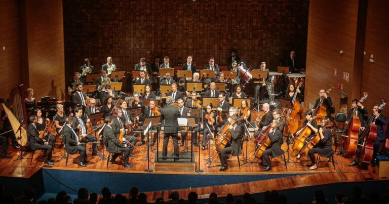 Uma orquestra se apresentando num palco.