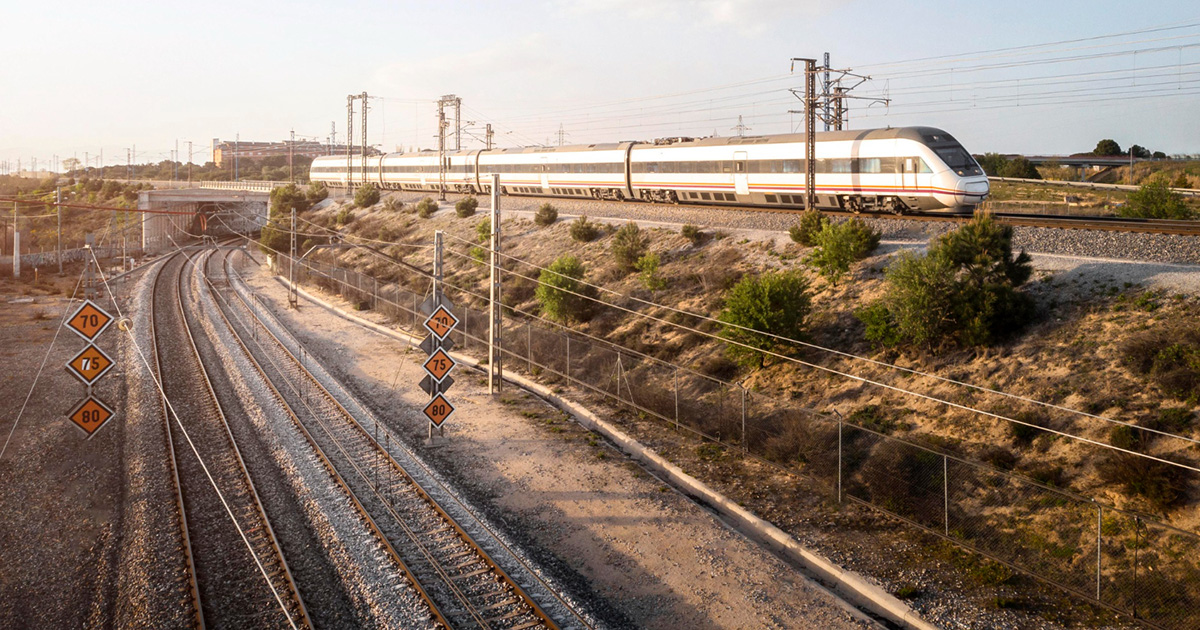 Ferrovia com um trem passando de fundo com uma vegetação verde ao redor