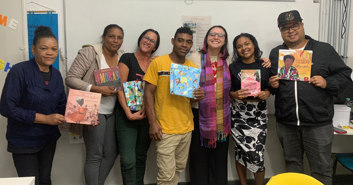 Sete estudantes do Cieja Butanã e Jade, educomunicadora, mostram livros em sala de aula.