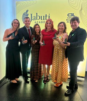 Seis autores do livro seguram o troféu do prêmio Jabuti, vestem traje social e estão sorrindo